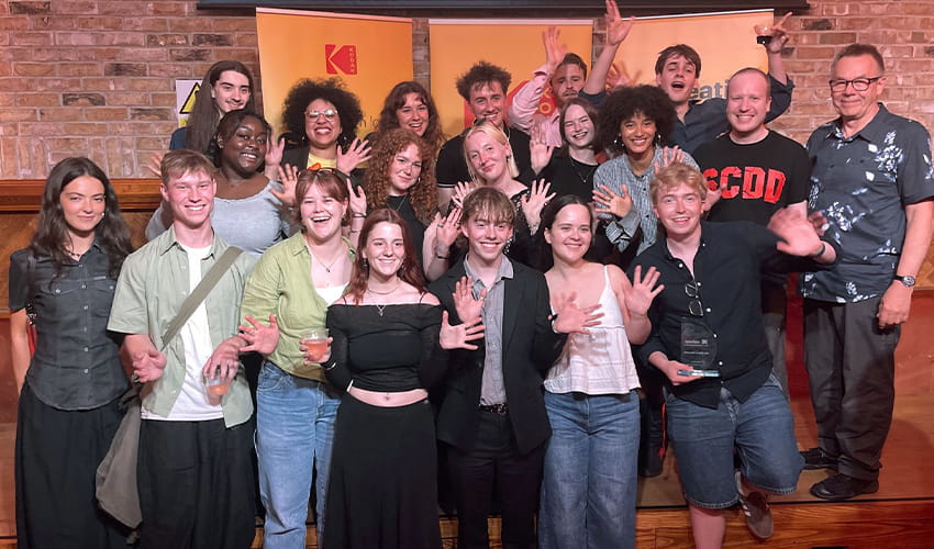 A group of celebrating students smile at the camera.