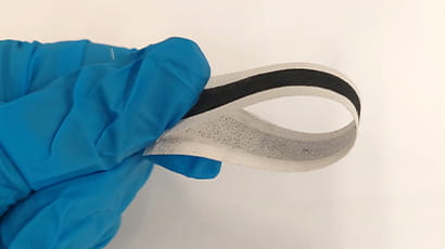 A strip of e-textile is held in a blue-gloved hand.